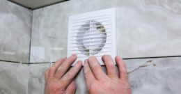 Installation d'une ventilation simple flux sur un mur carrelé, avec des mains fixant la grille de ventilation.
